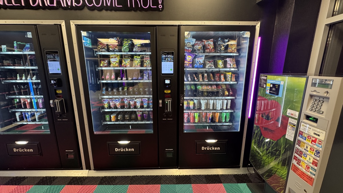 Automatenreihe im Store Vreden mit Snacks und Getränken hinter Glas, darüber ein Neonschriftzug